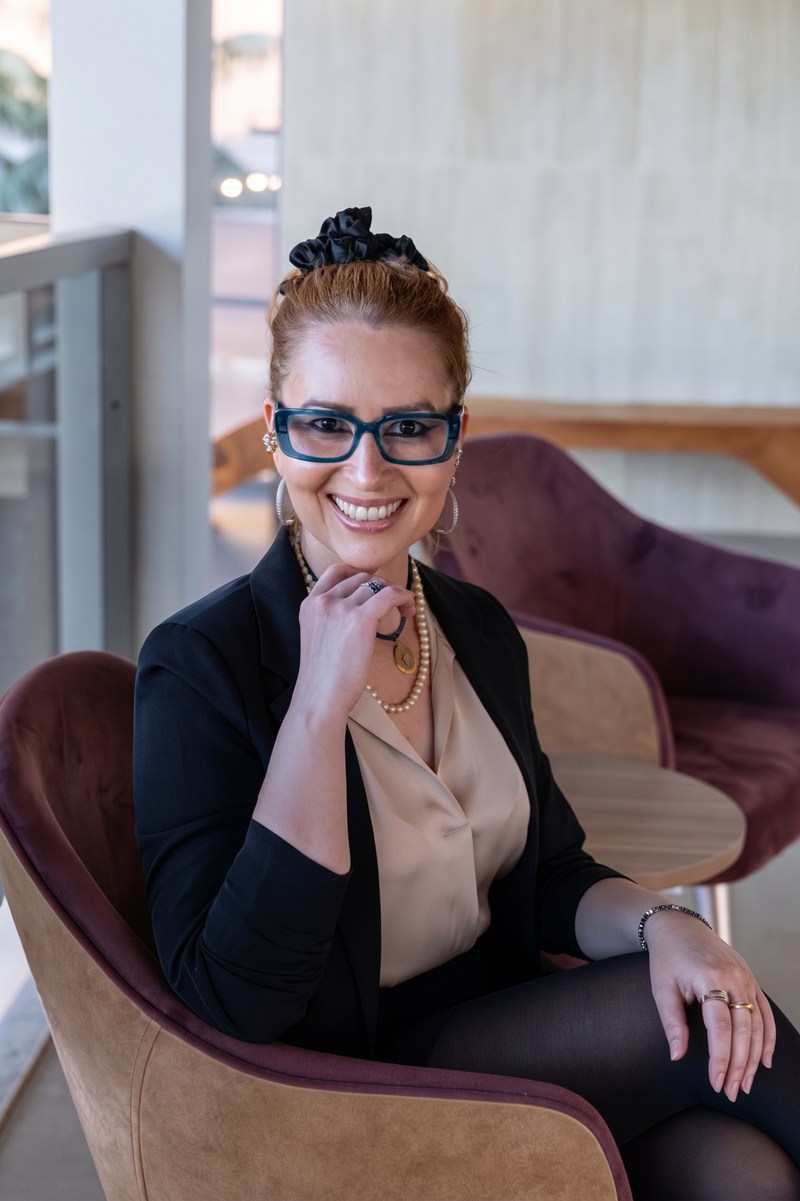 Renata Sellari Monteiro, sorrindo, de blazer preto e óculos